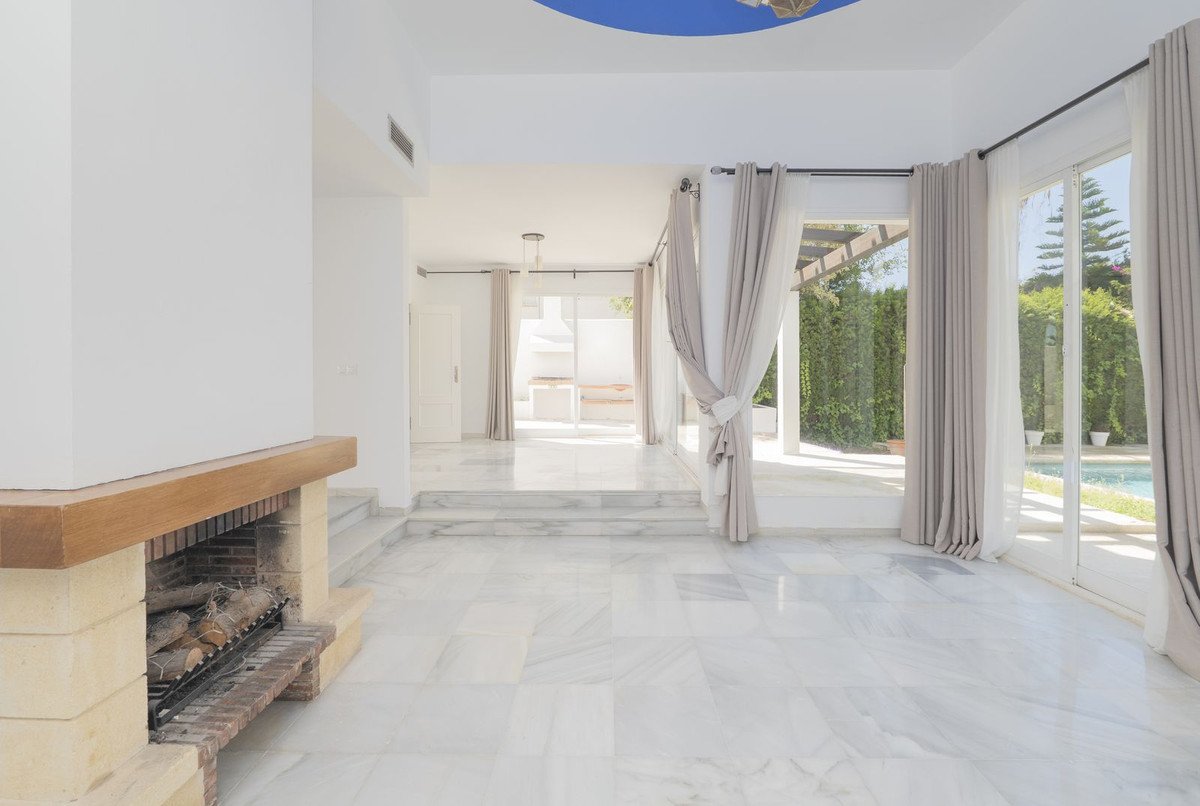 Spacious living room with marble floors, fireplace, and large windows overlooking a swimming pool and garden.