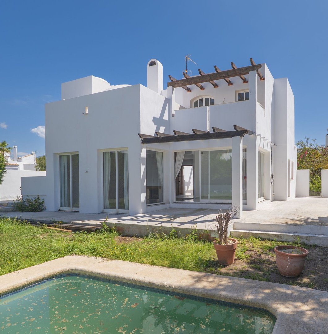 Modern white villa with a swimming pool, covered terrace, and large windows under a bright blue sky.