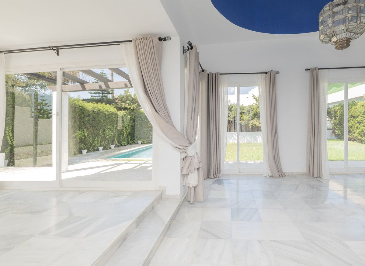 Spacious living room with marble floors and large windows overlooking a swimming pool and garden.