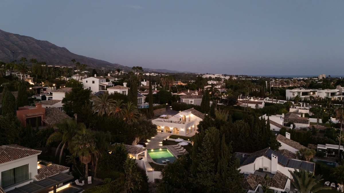 Luxury villa with a swimming pool, illuminated at dusk, set against a backdrop of mountains and lush greenery.