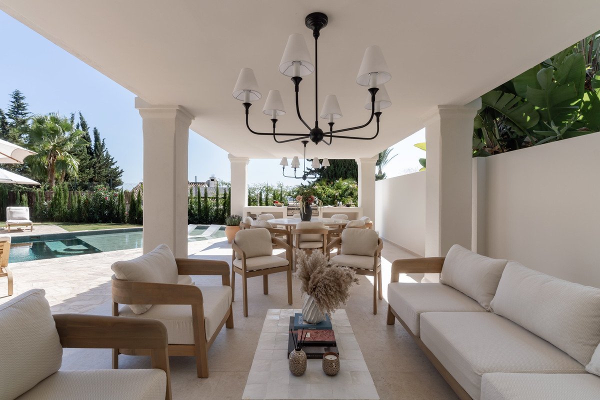 Covered patio with outdoor furniture, dining table, and a view of a swimming pool and lush greenery.