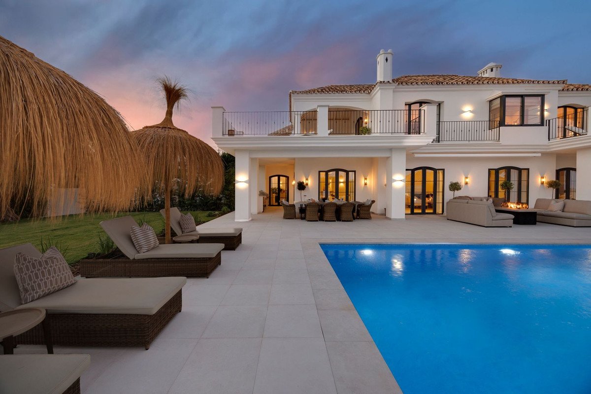 Luxurious villa with a swimming pool and terrace, featuring thatched umbrellas and loungers at sunset.