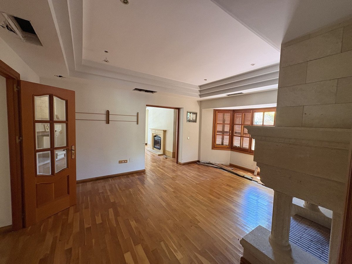 Spacious living room with polished wooden floors, a large stone fireplace, bay window, and a doorway leading to another room with a fireplace.
