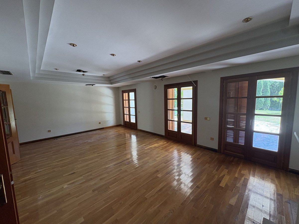Spacious living room with polished wooden floors and multiple glass doors opening to a lush green garden.