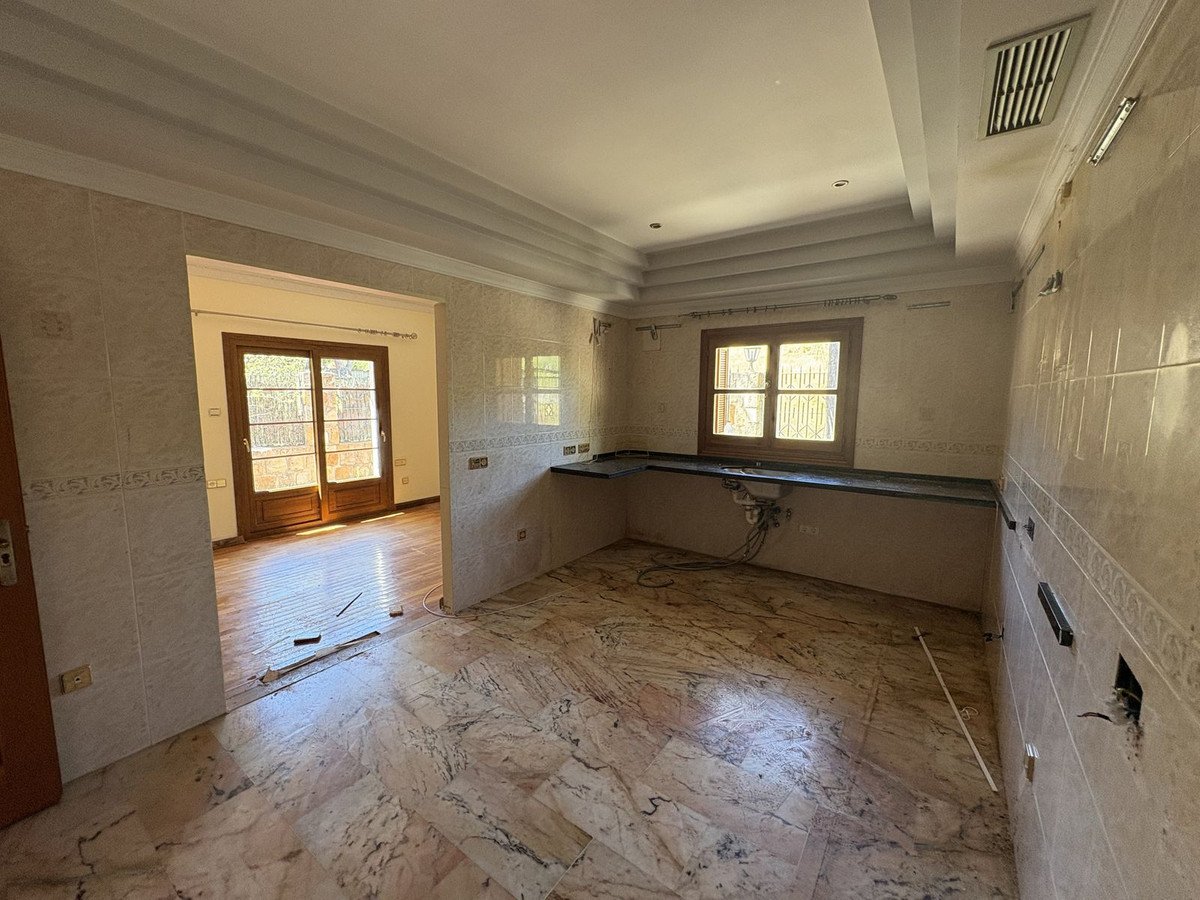 Spacious kitchen with marble floors, tiled walls, a dark countertop, and large windows letting in natural light.
