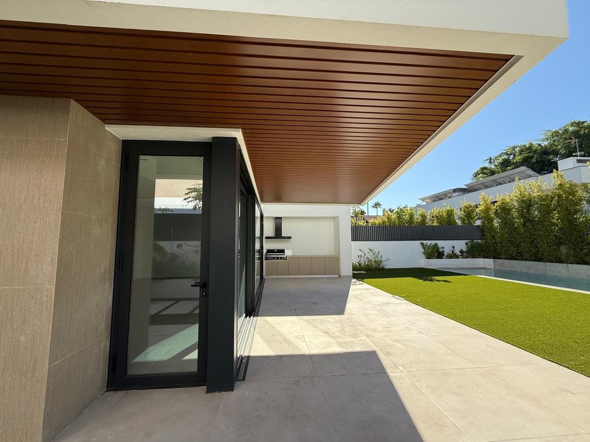 Modern patio with outdoor kitchen, artificial lawn, swimming pool, and sleek architectural features on a sunny day.