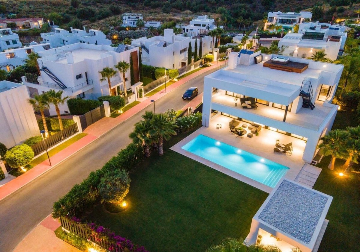 Luxury modern villa with swimming pool, green lawn, and outdoor seating areas. Hills in background.