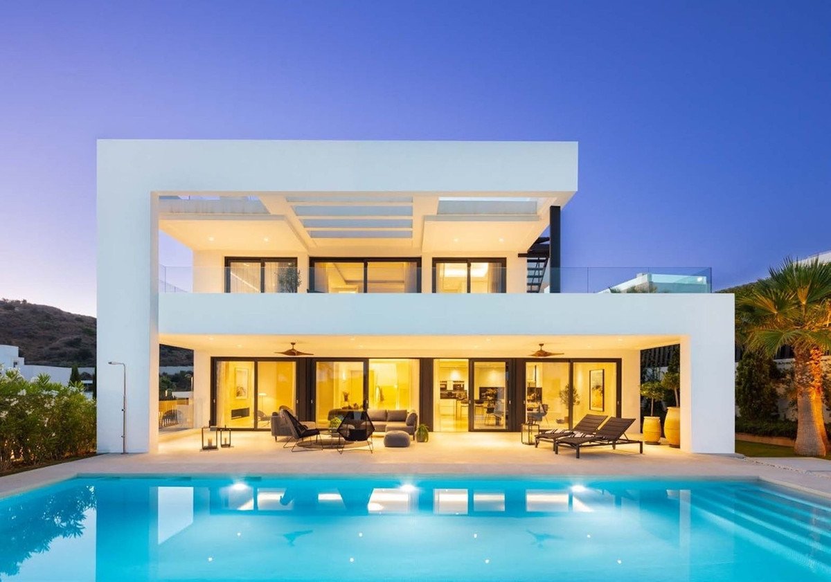 A modern luxury villa with a swimming pool and outdoor terrace at sunset. Features large windows and a sleek architectural design.