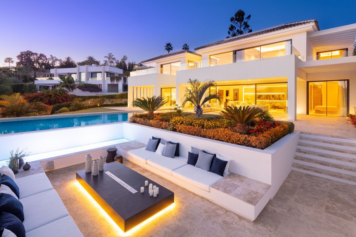 Luxurious modern villa at dusk with swimming pool, outdoor lounge seating, and illuminated features.
