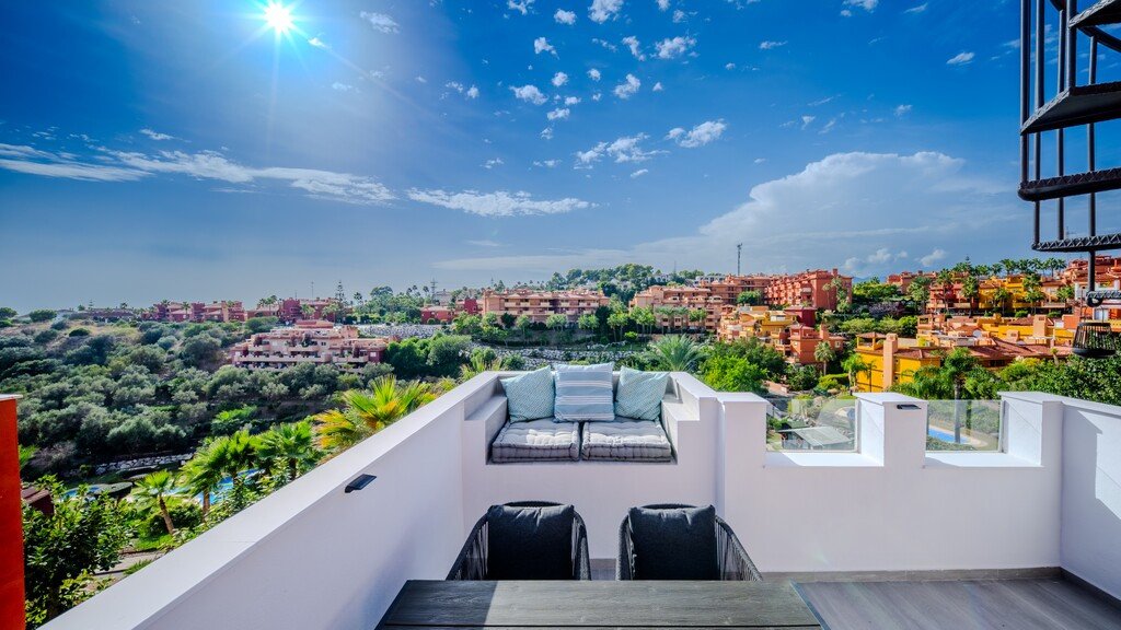 Rooftop terrace with seating, panoramic view of town and greenery under sunny sky