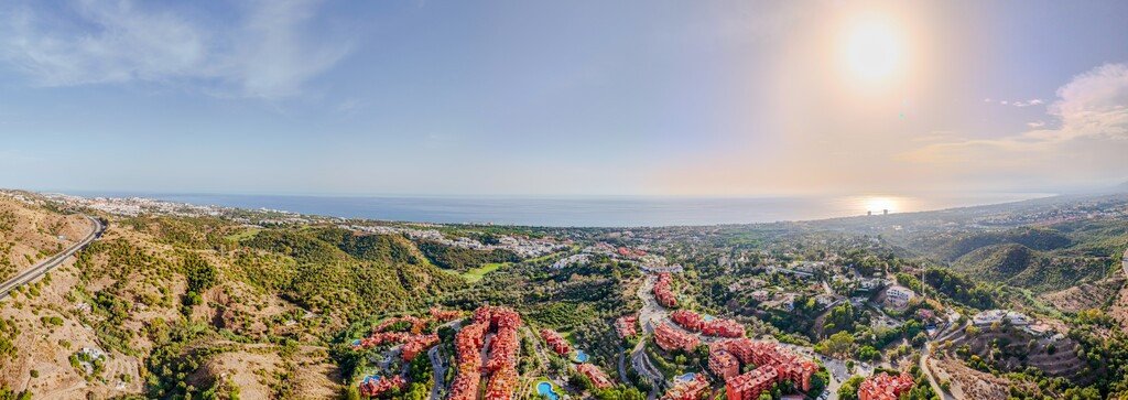 Aerial view of a villa with a pool, surrounded by green hills and overlooking the ocean.