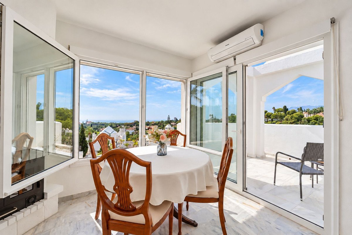 Dining area with a round table and chairs, large windows offering a sea and town view, and access to a terrace.