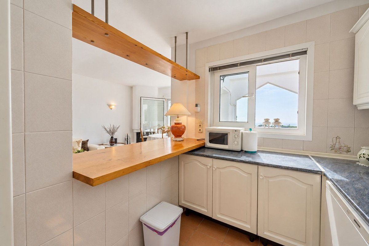 Kitchen with breakfast bar overlooking a living area and a window with a distant sea view and rooftops.