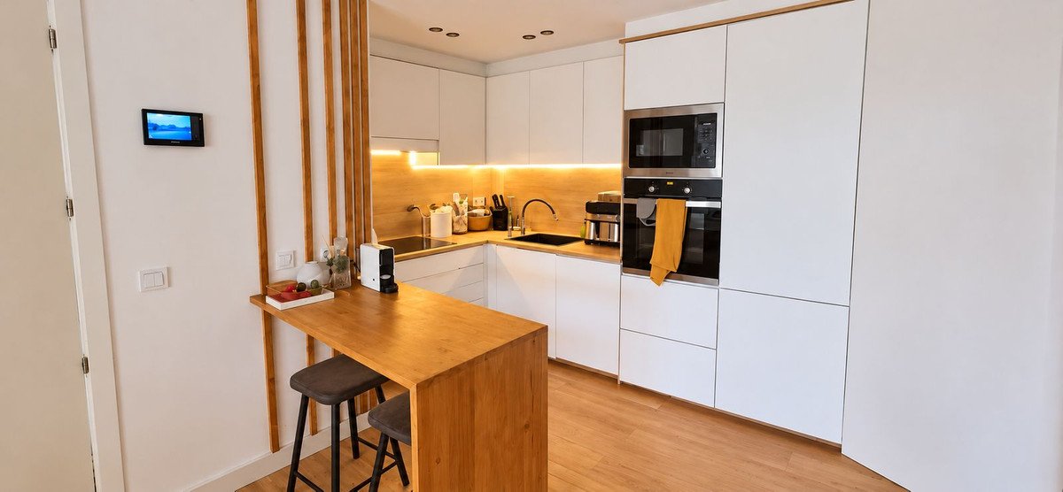 Modern white kitchen with a wooden breakfast bar, stainless steel appliances, and ambient lighting.