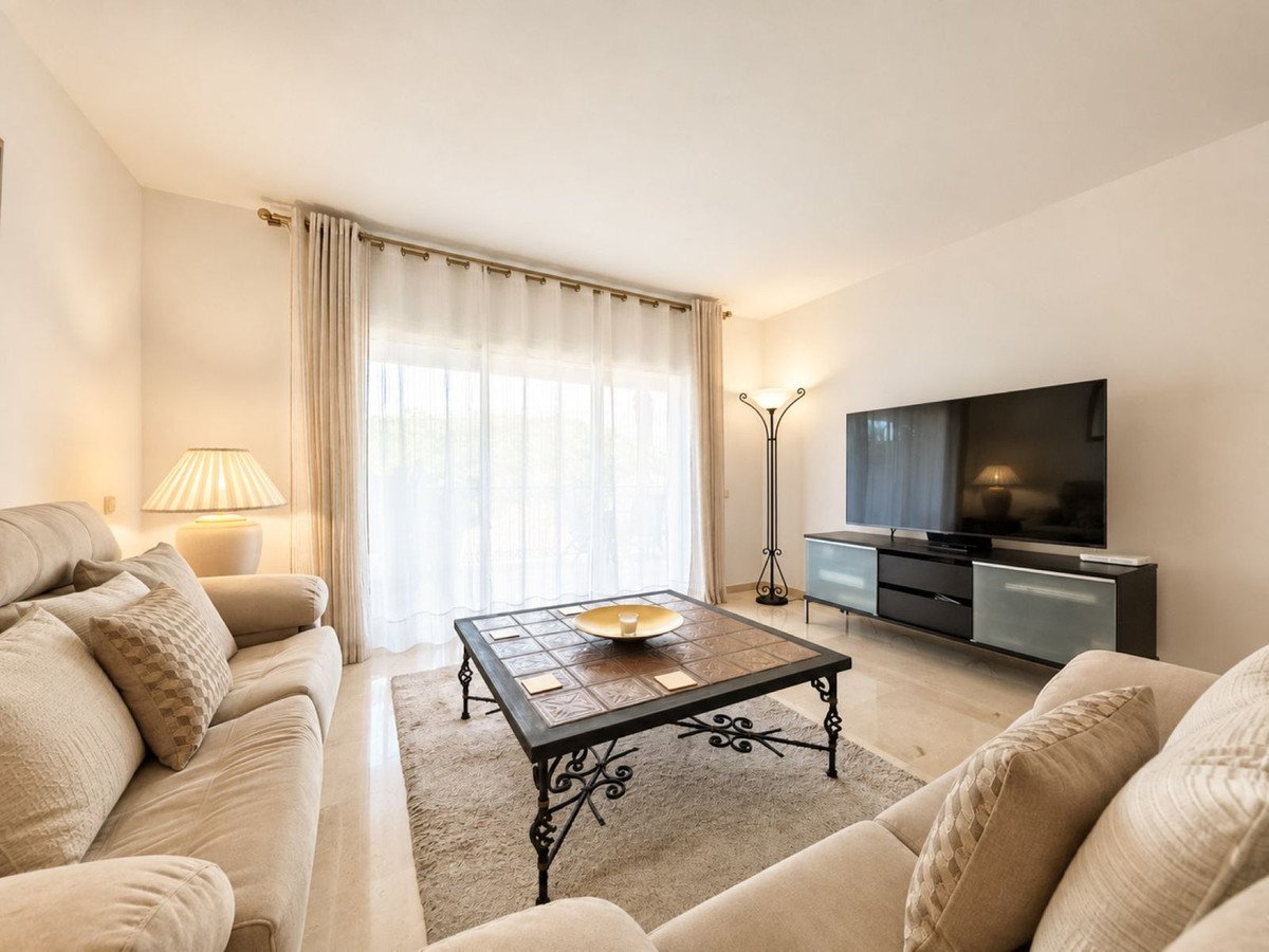 A bright living room with a beige sofa, a coffee table, and a large flat-screen TV mounted on the wall.