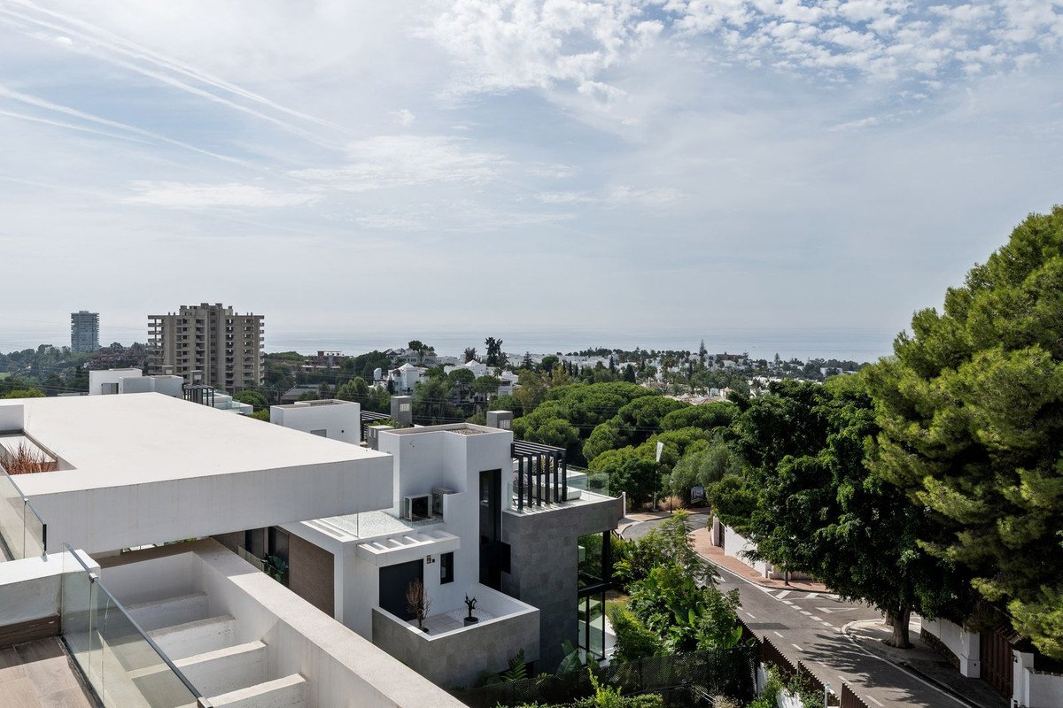 Modern villa with multiple levels and balconies, offering a panoramic view of the sea and surrounding greenery.