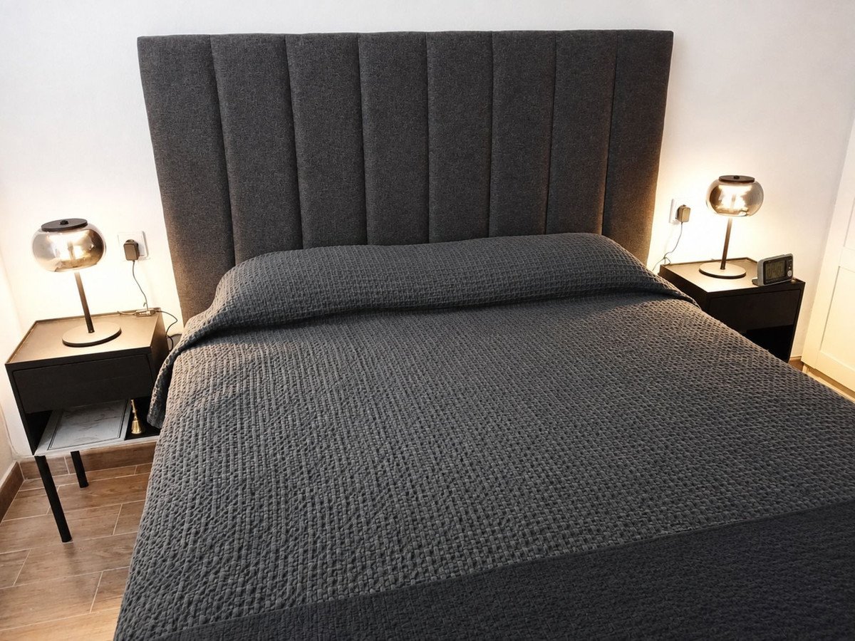 Modern bedroom with a large bed, tall upholstered headboard, and two bedside tables with stylish lamps.