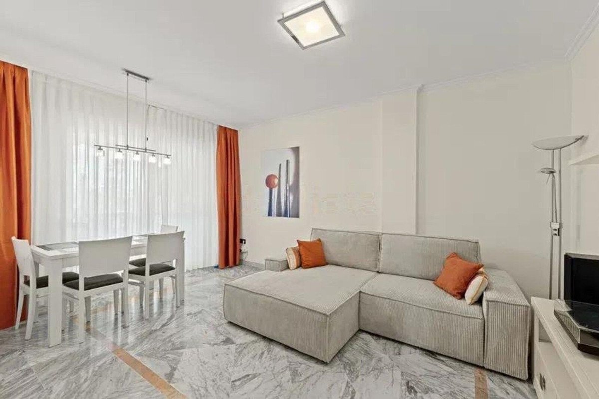 A modern living and dining area with a sectional sofa, dining table with chairs, and large windows with orange curtains.