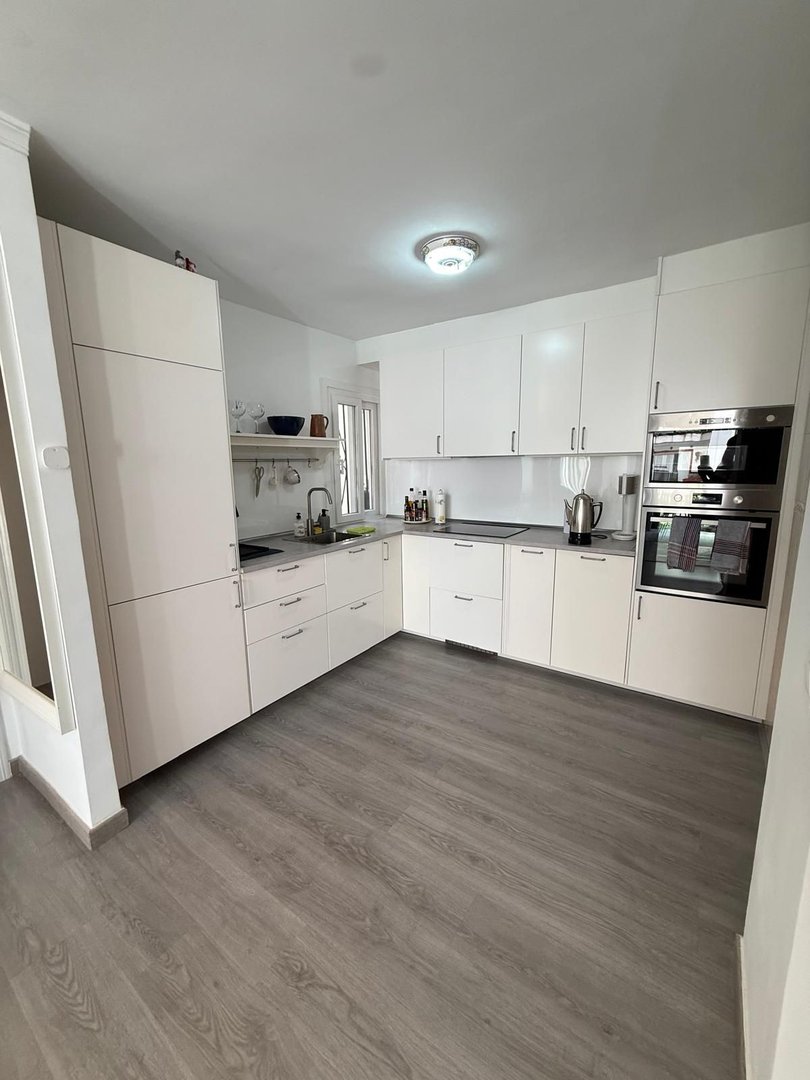 A modern white kitchen with integrated appliances and sleek cabinetry, featuring a grey wood-look floor.