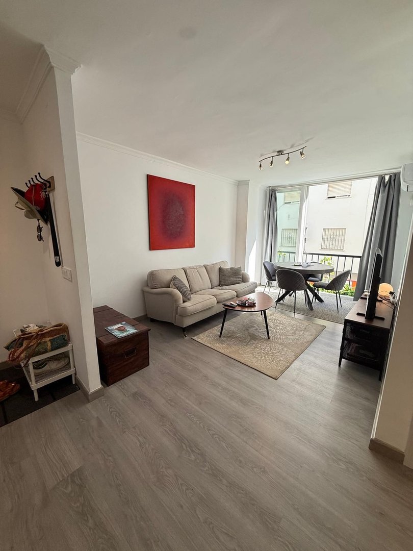 Cozy living room with a sofa, coffee table, dining area, and balcony access overlooking a building.