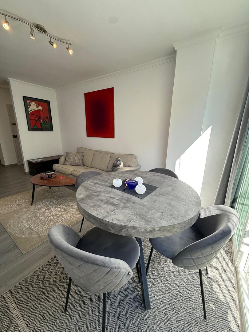 Modern dining area with a round concrete table, velvet chairs, and contemporary art on the walls.