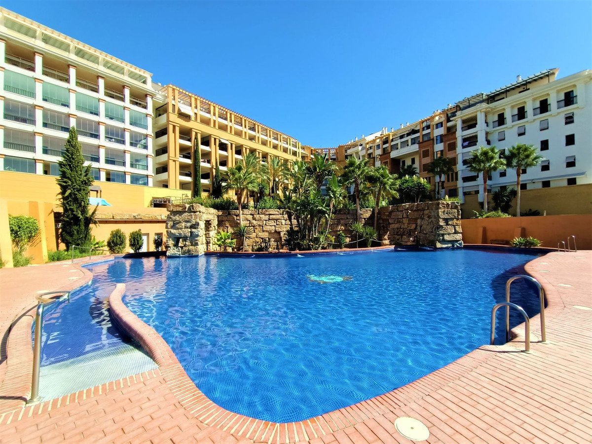 Outdoor swimming pool with clear blue water, surrounded by apartment buildings and palm trees.