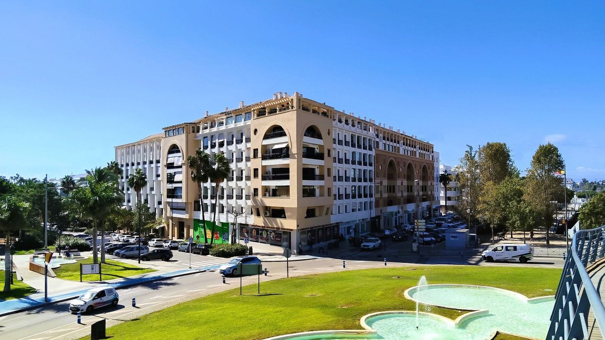 Modern apartment building with palm trees and fountain in sunny urban setting
