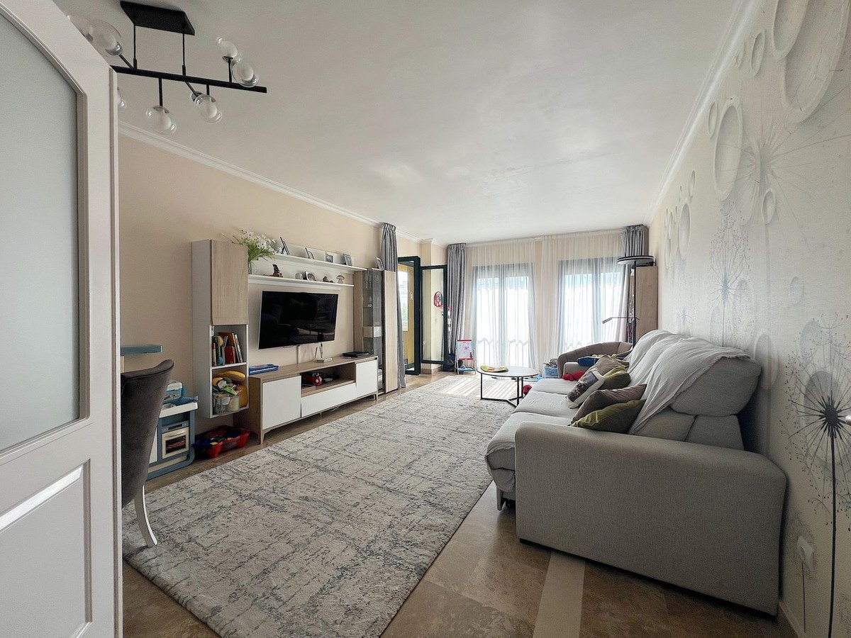 Spacious living room with a modern sofa, TV unit, large rug, and decorative wallpaper. Bright and airy with large windows.