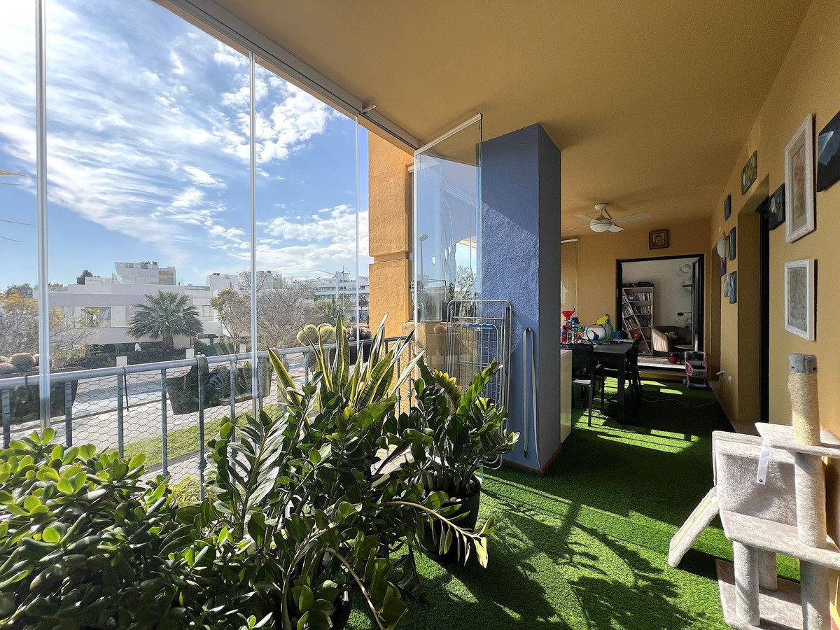 Enclosed balcony with artificial turf, plants, and a view of the city under a cloudy blue sky.