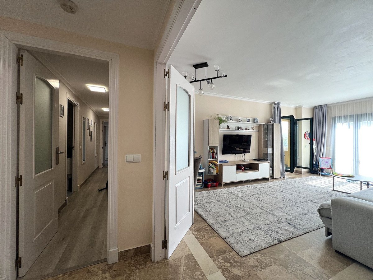 Spacious living room with TV, entertainment unit, large rug, and balcony doors leading to an outdoor view.