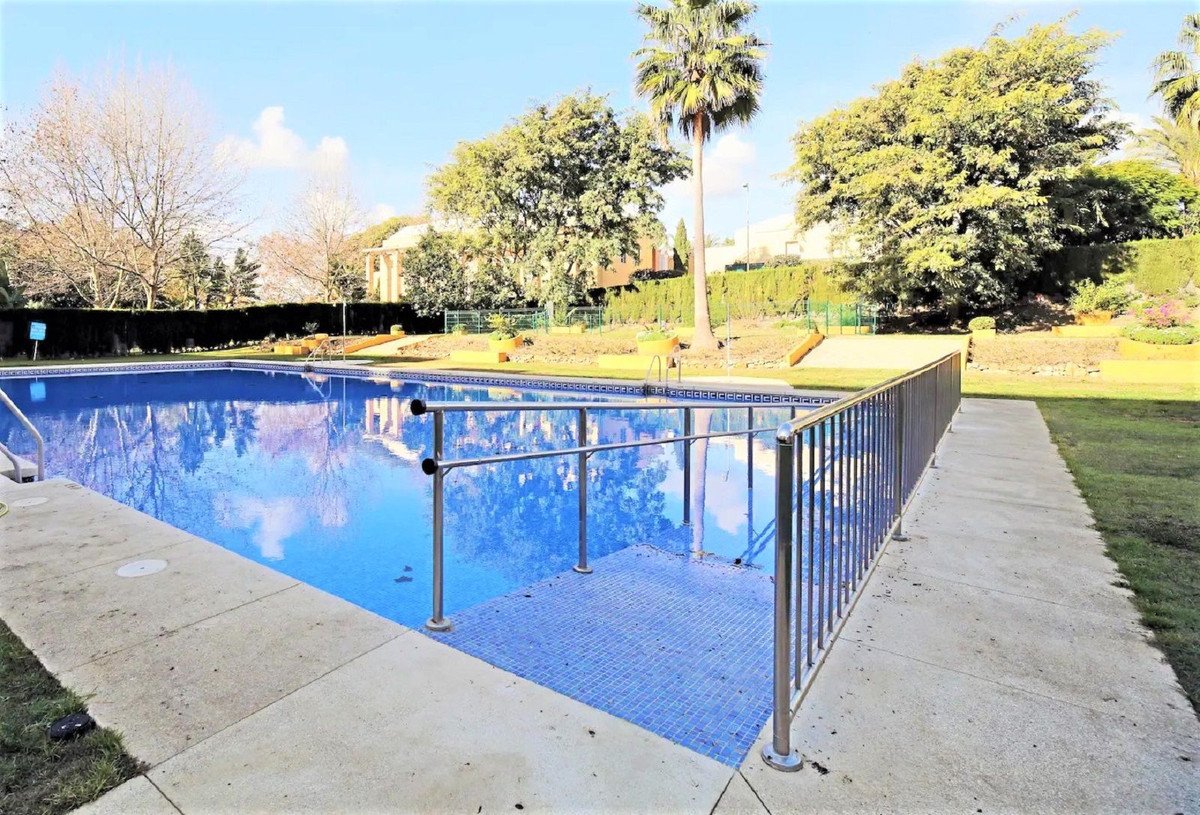 Outdoor swimming pool with clear blue water, surrounded by garden and trees.