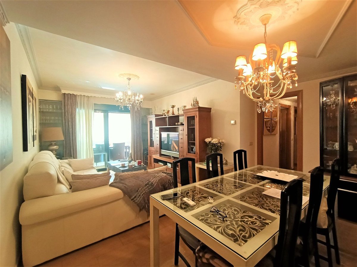 Open-plan living and dining room with chandeliers, sofa, and glass dining table