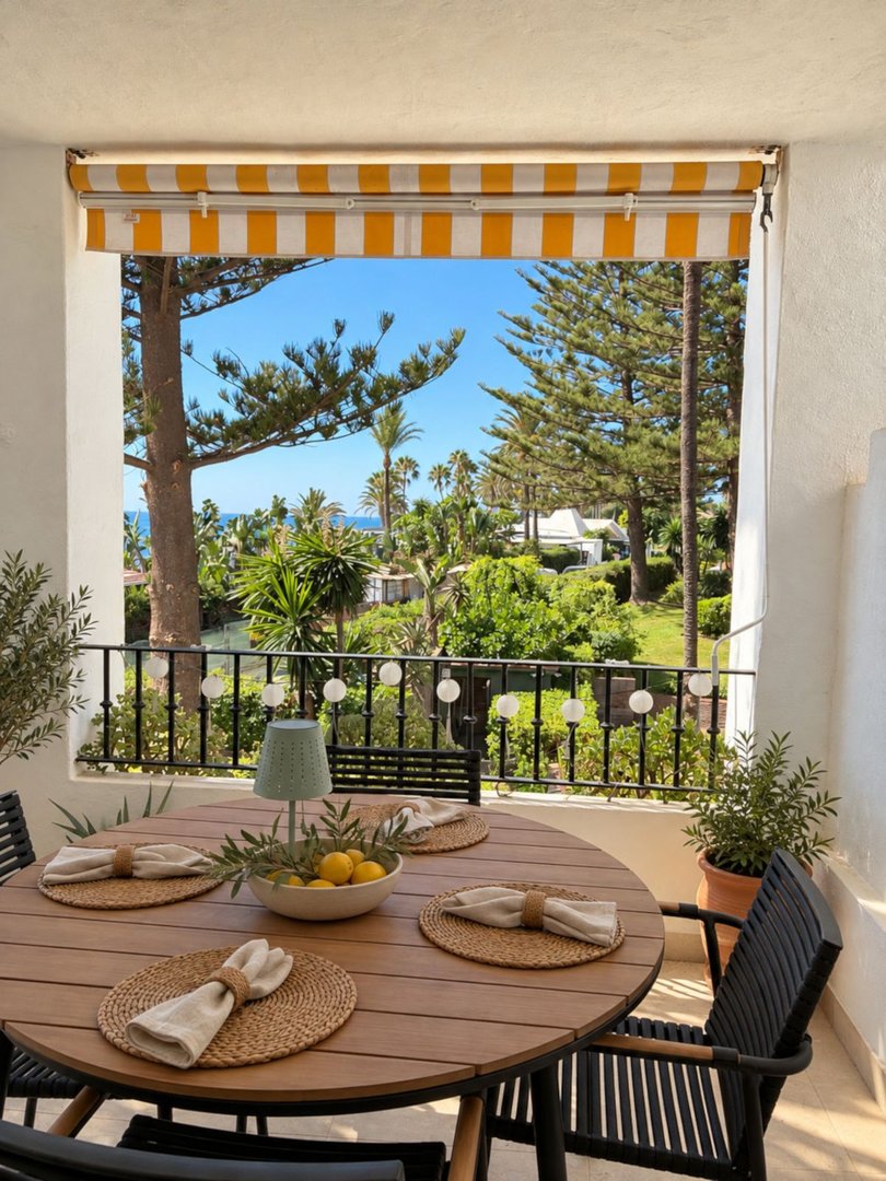 Outdoor dining table on a balcony with a beautiful sea view and lush greenery under a sunny sky.