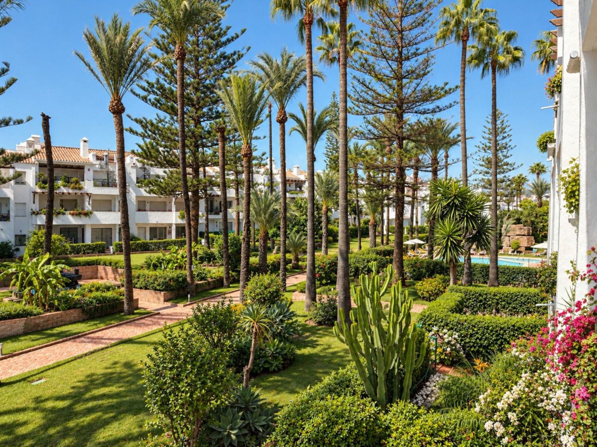Lush tropical gardens with palm trees, exotic plants, and a swimming pool visible in the background.