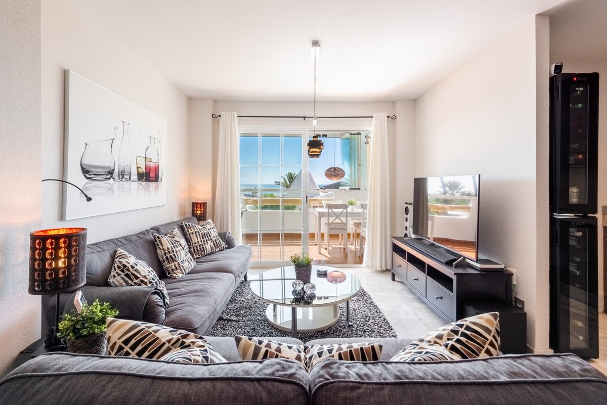 Modern living room with grey sofa, large windows with sea view, dining area on balcony and wine cooler.