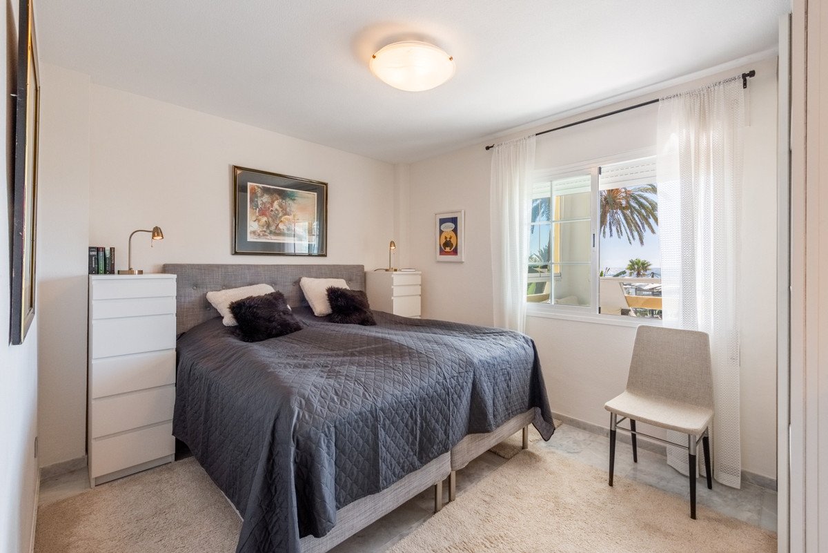 Bedroom with a large bed, a dresser, and a window showing a balcony, sea view, and palm trees.