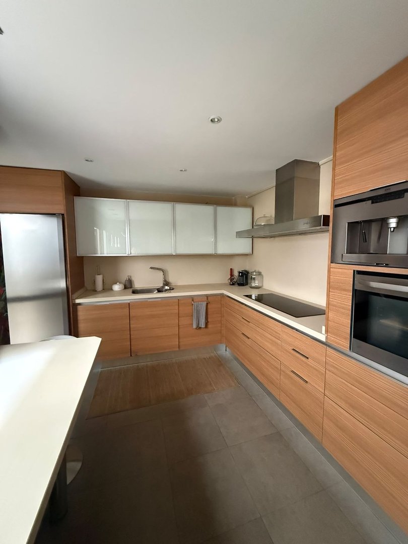 Modern kitchen with wooden cabinets, stainless steel appliances, and a white countertop island.