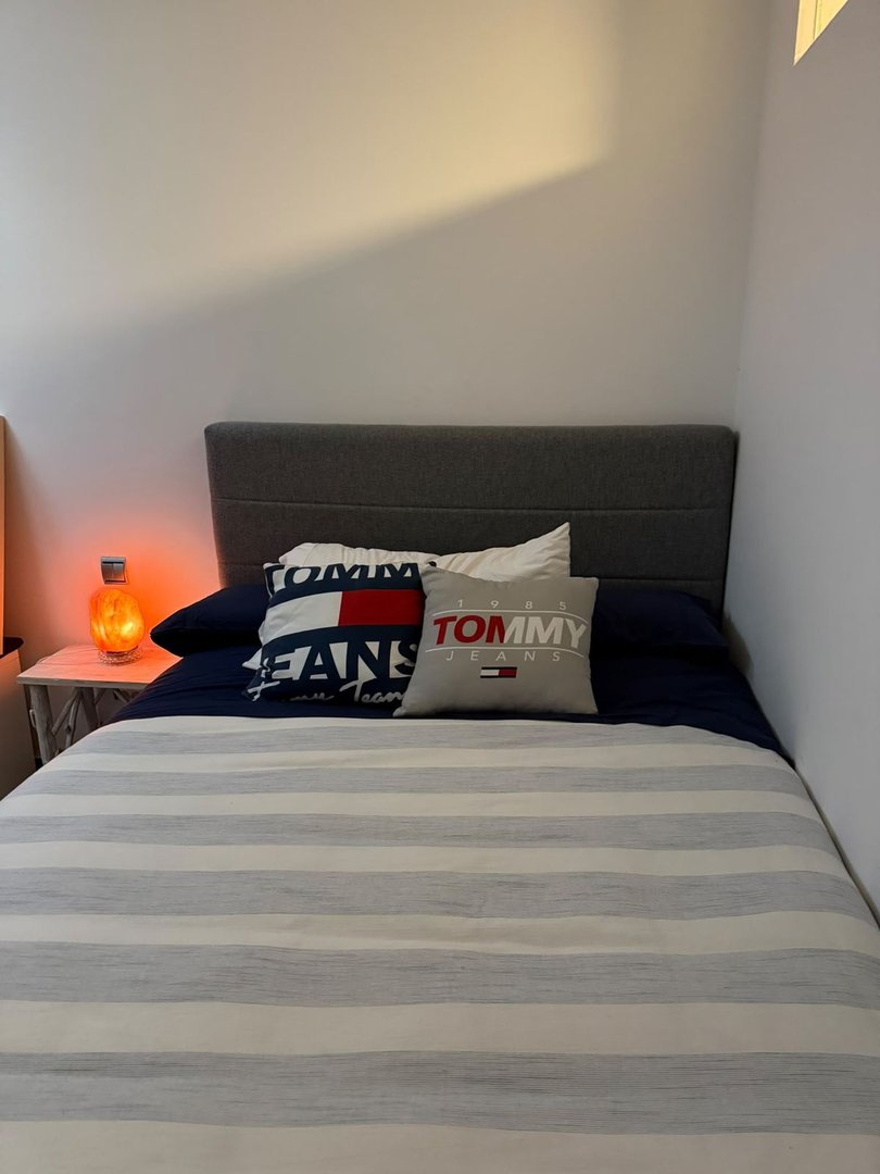 Small bedroom with striped bedspread, Tommy Jeans pillows, and orange lamp