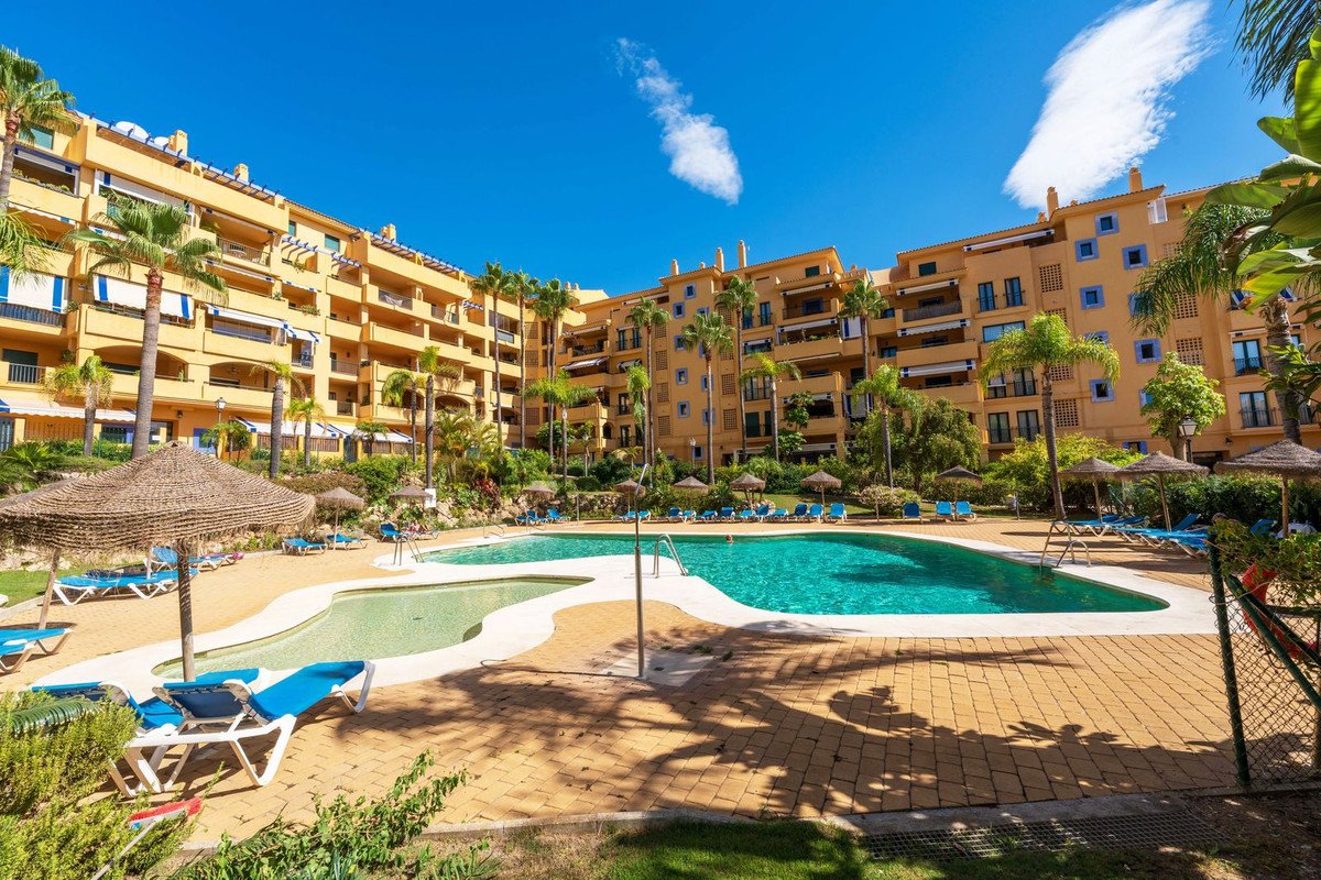 Luxury apartment complex with a large, inviting swimming pool and sun loungers on a sunny day.
