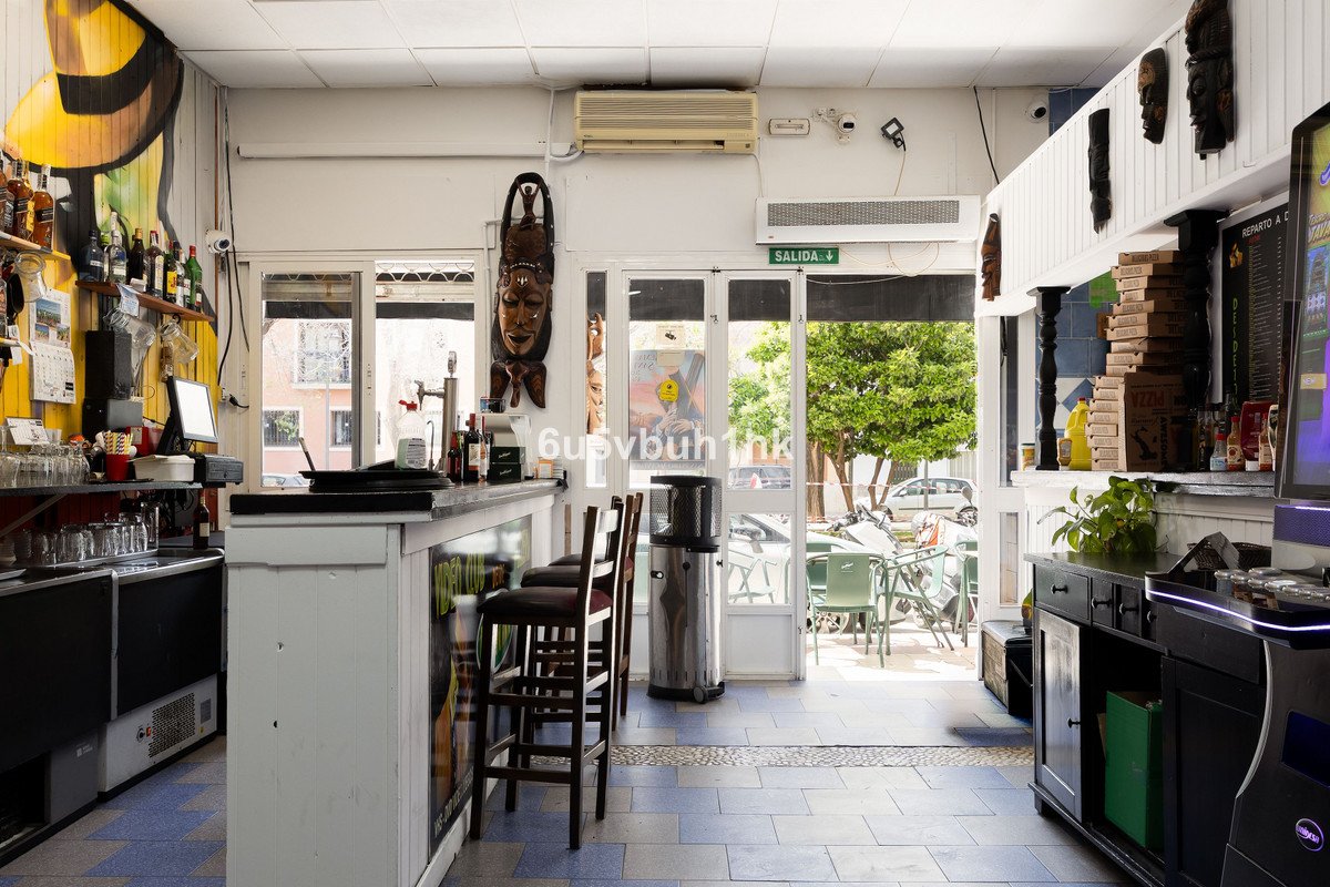 Interior of a bar with a counter, stools, and an exit leading to outdoor seating with trees and cars visible.