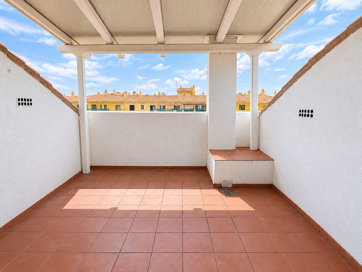 A sunny rooftop terrace with terracotta tiles, white walls, and a view of yellow buildings.