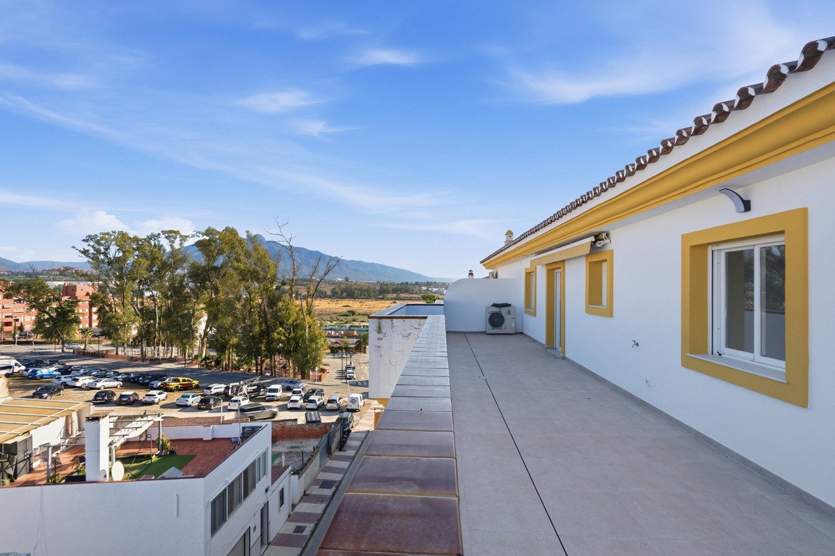Spacious terrace with a view of mountains and a parking lot below, featuring white walls and yellow window frames.