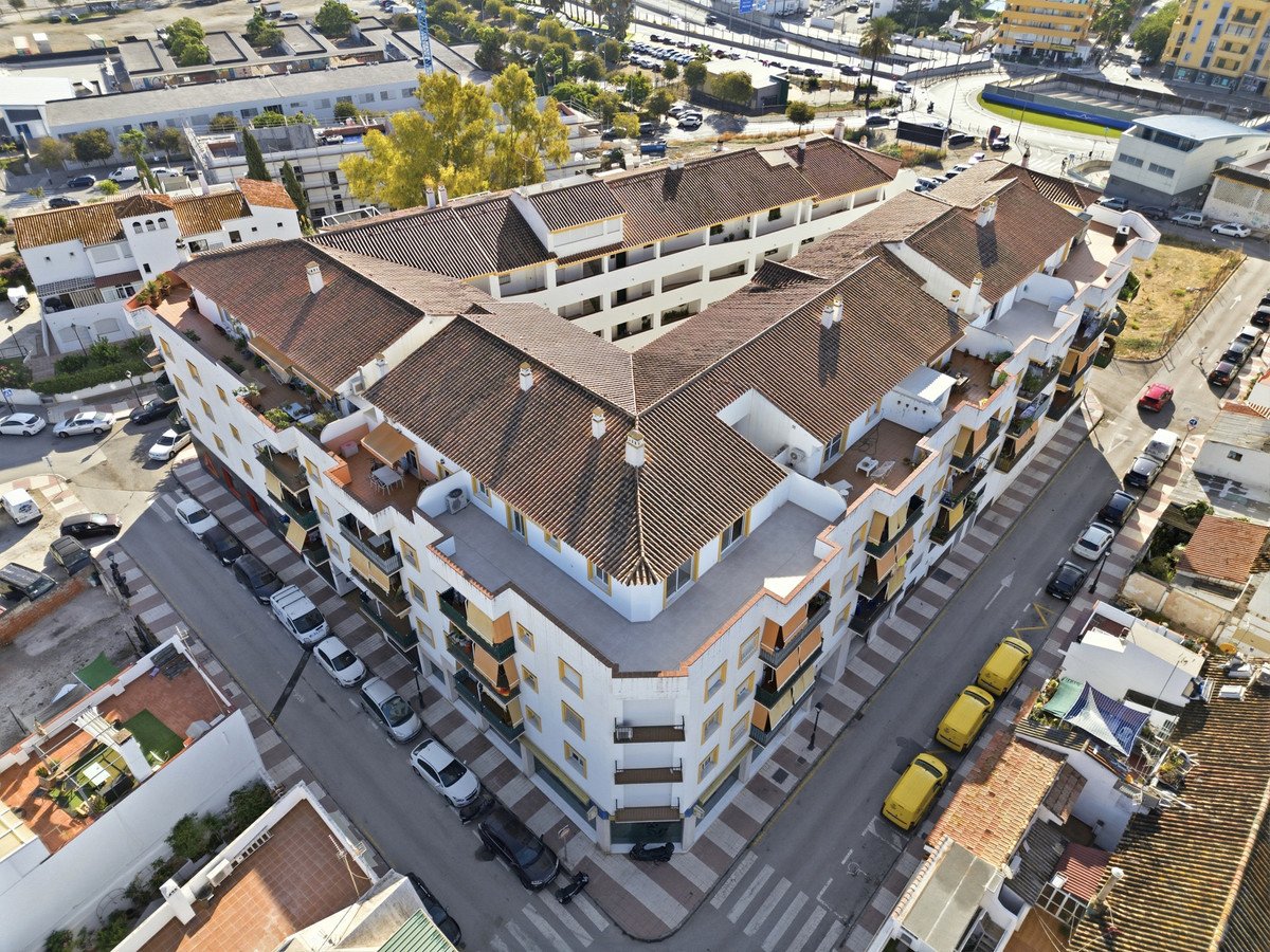 Aerial view of a multi-story apartment building with balconies, terraces, and surrounding urban street with parked cars.