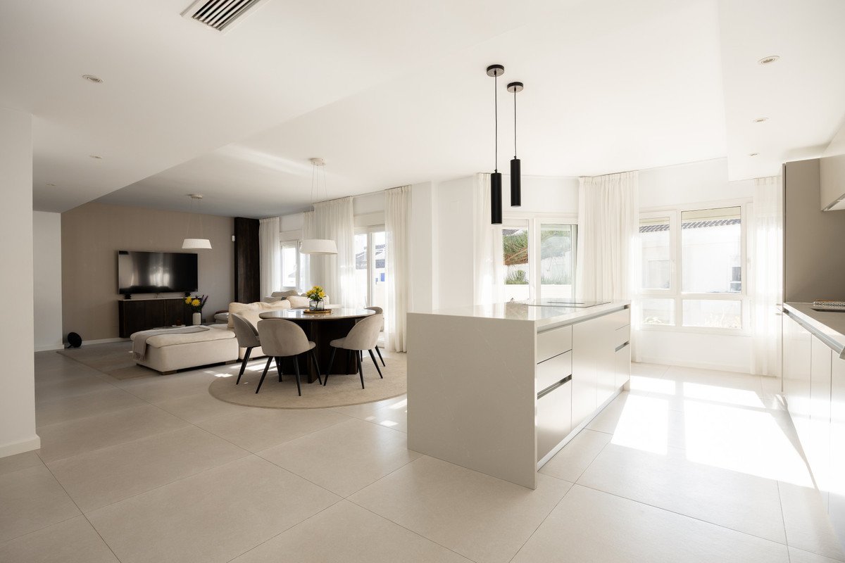 Modern open-plan living, dining, and kitchen space with white cabinetry and large windows