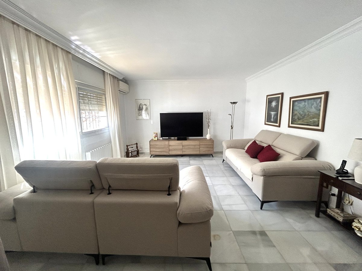 Cozy living room with two beige sofas, a TV on a wooden stand, and light curtains covering a window.