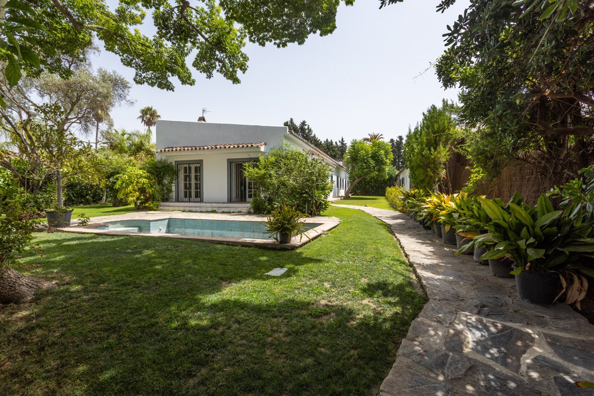 White villa with a small pool, lush green garden, and stone pathway.