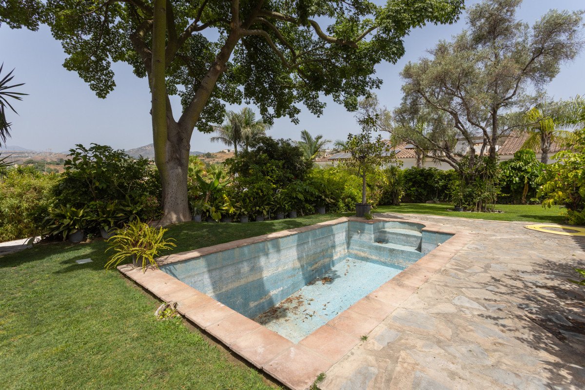 Empty outdoor swimming pool in a lush garden with trees and distant hills