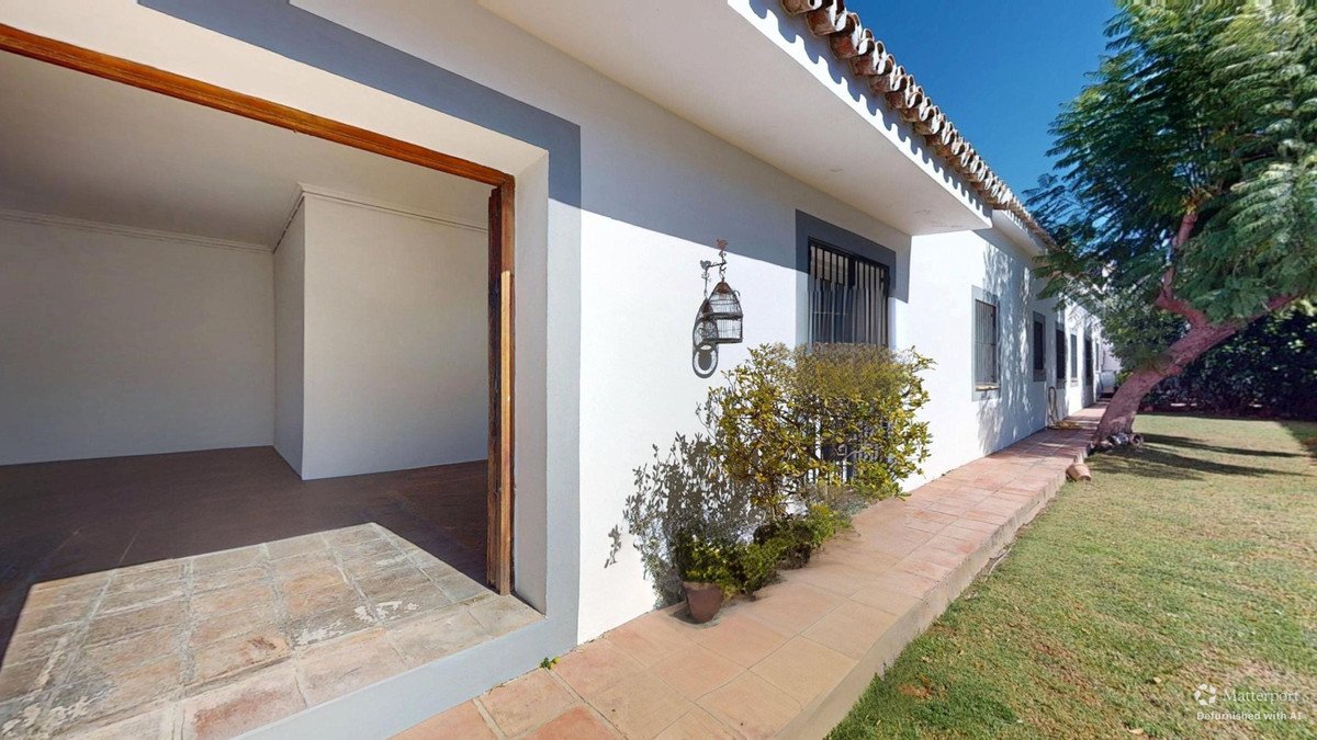 White villa exterior with open patio, tiled floor, and garden view.