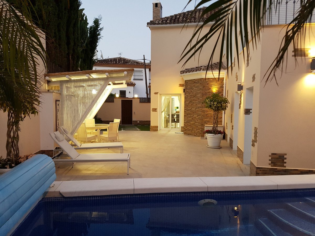 Outdoor patio with lounge chairs, dining table under a canopy, and a swimming pool at dusk.