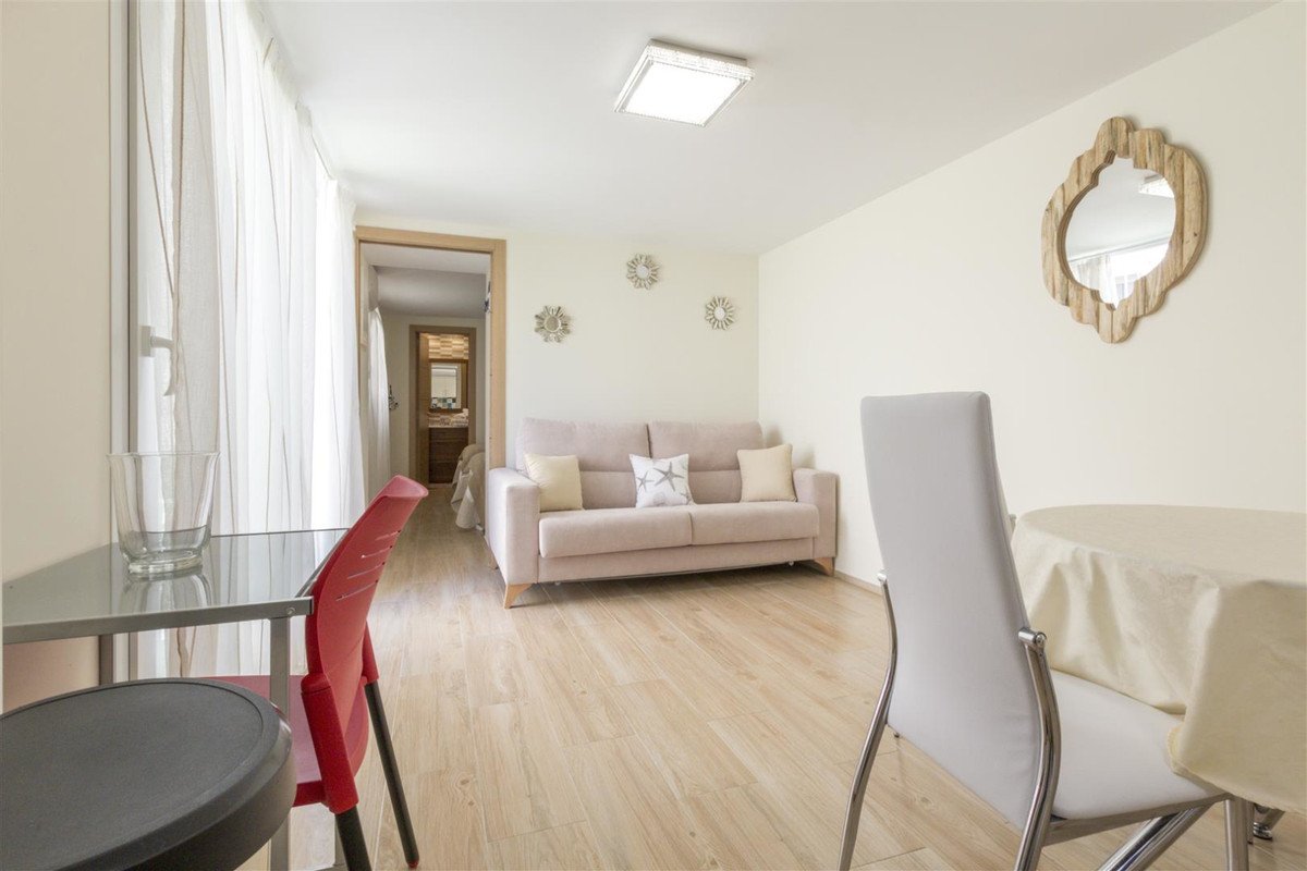 A light-filled living room with a sofa, dining area, and view into a bathroom and bedroom.